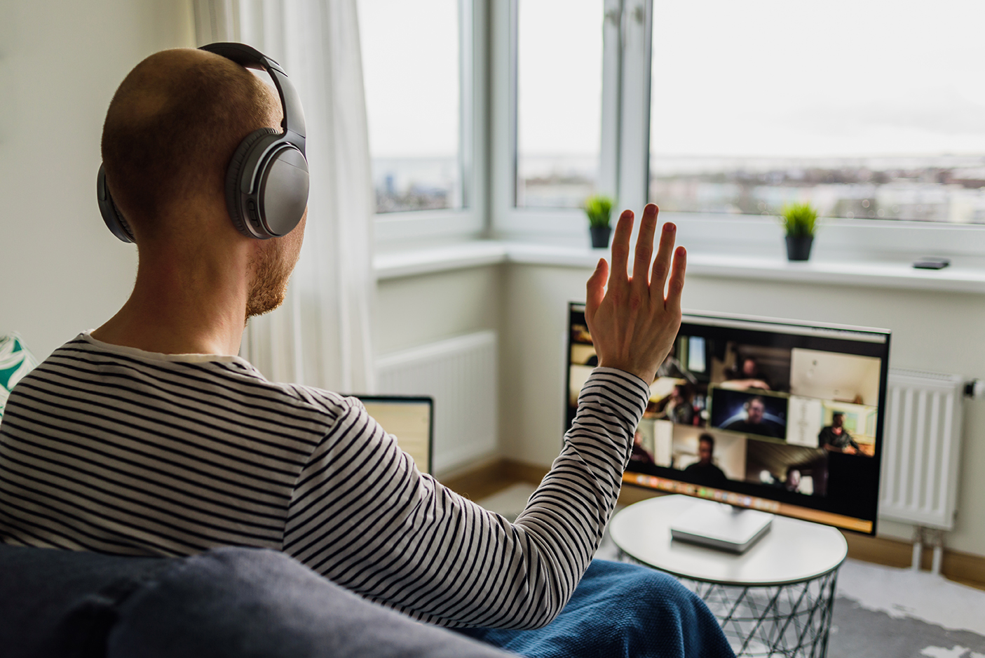 Man having video call with colleagues Man in headphones working from home. Having a video call meeting with his team on big monitor